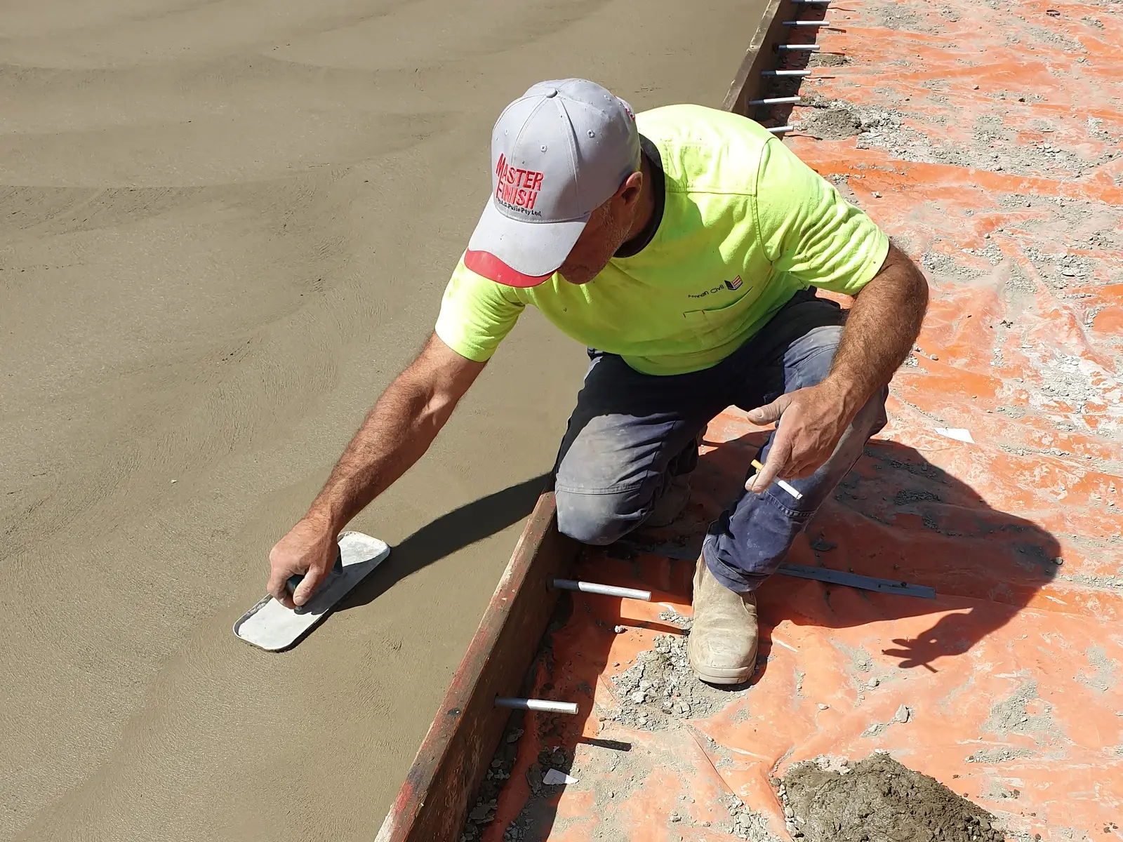 Concreter hand-finishing the edge of a freshly poured slab along the formwork