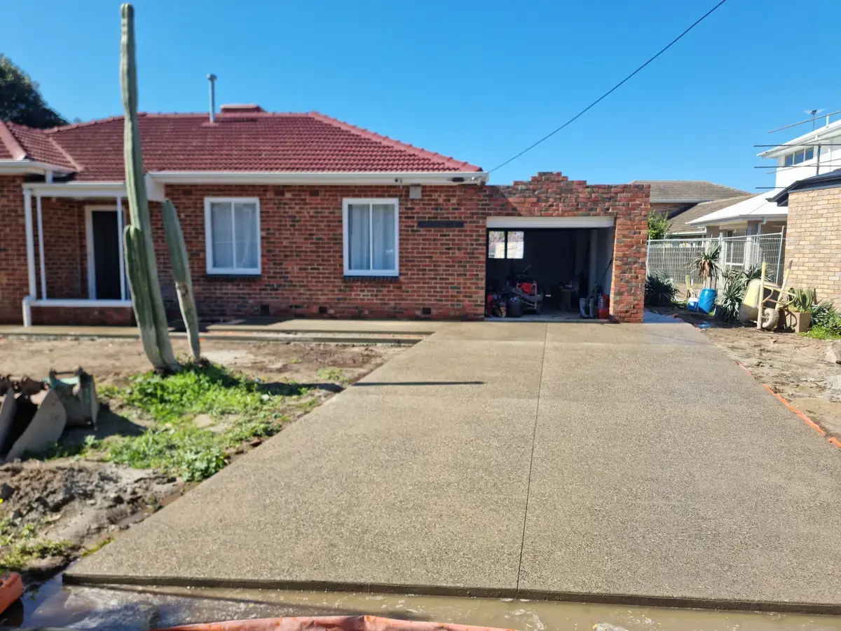 Newly finished exposed aggregate concrete driveway with a centre control joint, leading to the garage of a red brick home