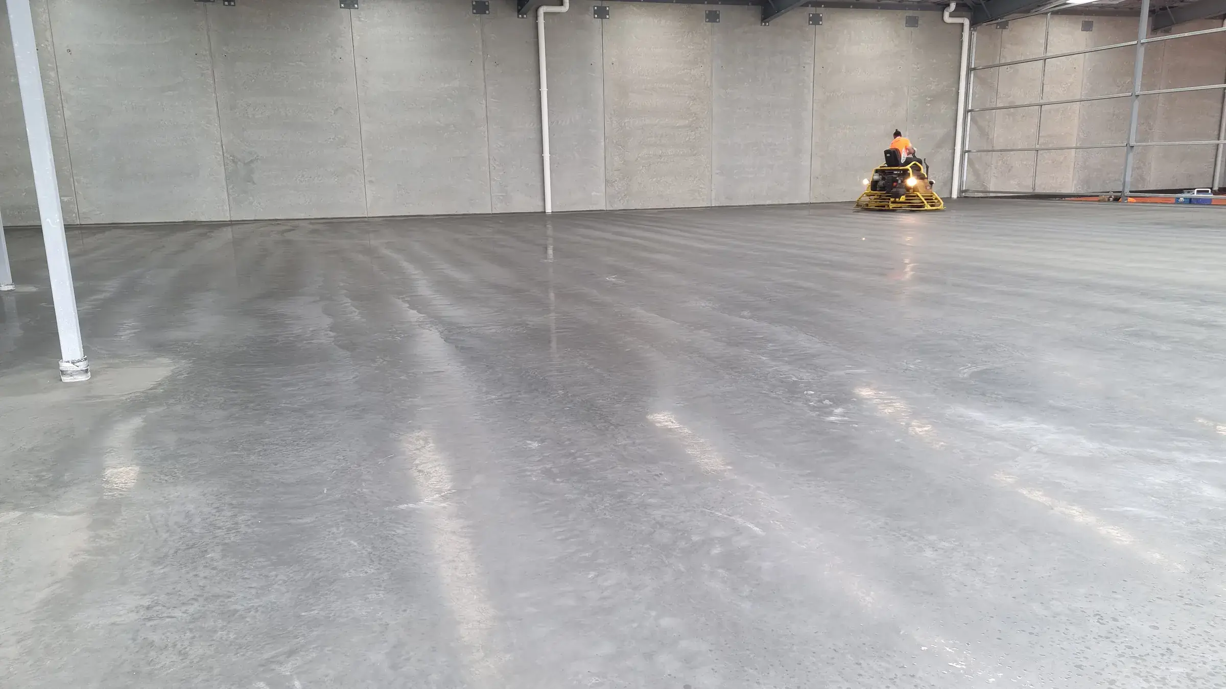 Operator on a ride-on power trowel finishing a large burnished concrete warehouse floor