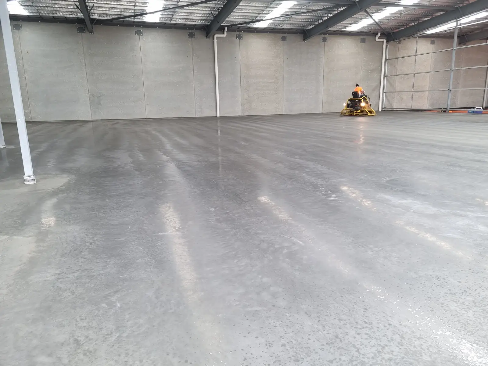 Burnished concrete warehouse floor in Largs North, with a ride-on power trowel working at the far wall